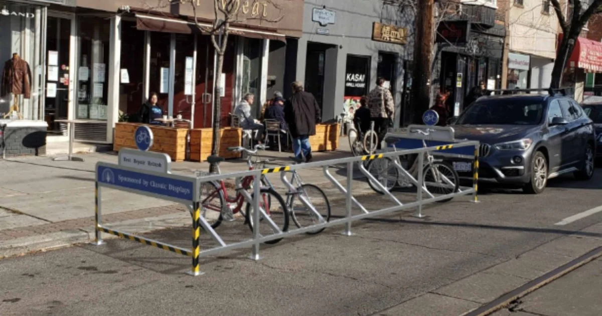 Street-side bike rack with multiple bicycles parked outside a row of urban shops.